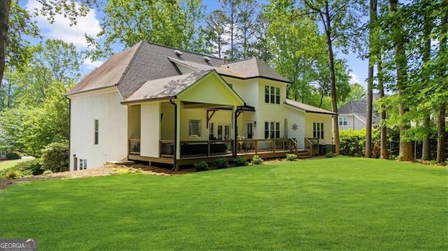 rear view of house featuring a lawn, roof with shingles, a wooden deck, and stucco siding