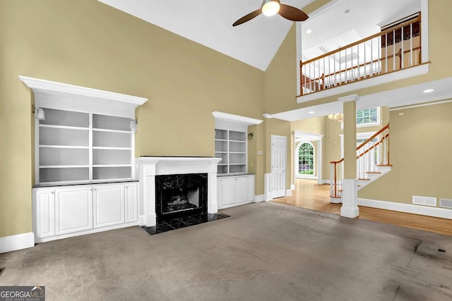 unfurnished living room featuring a ceiling fan, baseboards, stairway, a towering ceiling, and a high end fireplace