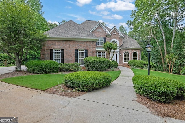 view of front of home with brick siding, a front lawn, and roof with shingles