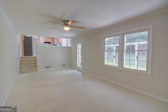 empty room with ceiling fan, light colored carpet, baseboards, visible vents, and ornamental molding