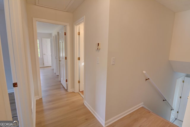 hallway featuring light wood-style floors, attic access, baseboards, and an upstairs landing