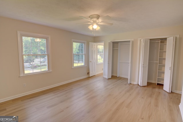 unfurnished bedroom featuring light wood-style floors, a ceiling fan, multiple closets, and baseboards