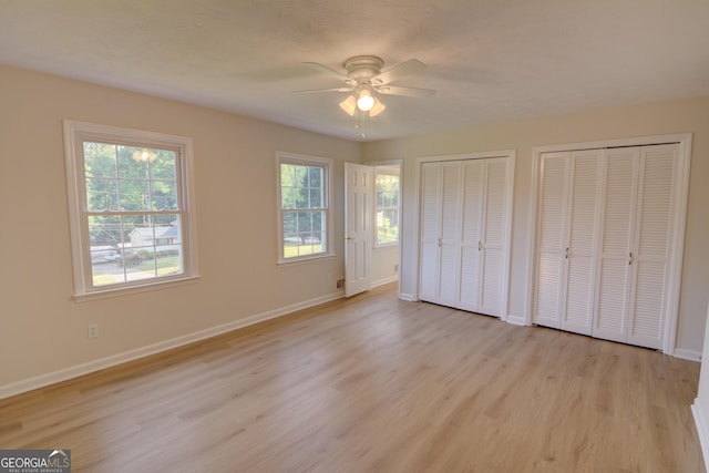 unfurnished bedroom featuring baseboards, multiple closets, ceiling fan, and light wood finished floors