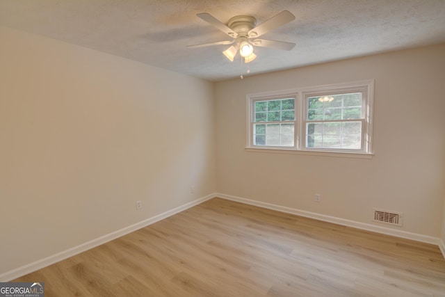 spare room featuring a textured ceiling, light wood-style flooring, a ceiling fan, baseboards, and visible vents