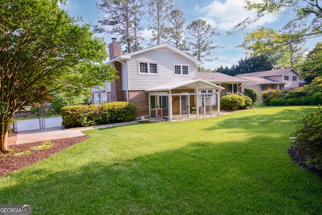rear view of property with a chimney, a lawn, a gate, a sunroom, and brick siding