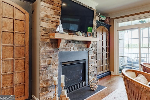 interior space with crown molding, baseboards, a stone fireplace, and wood finished floors