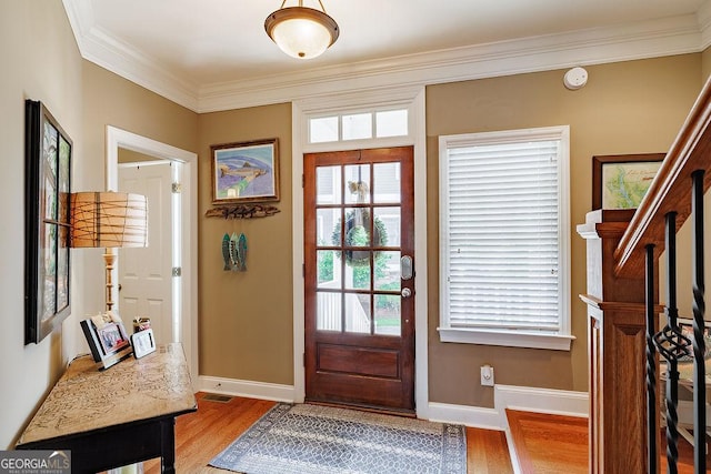 foyer featuring baseboards, ornamental molding, light wood-style flooring, and visible vents