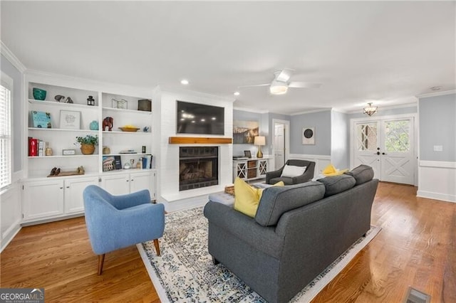 living room featuring a fireplace with raised hearth, ceiling fan, ornamental molding, and light wood-style flooring