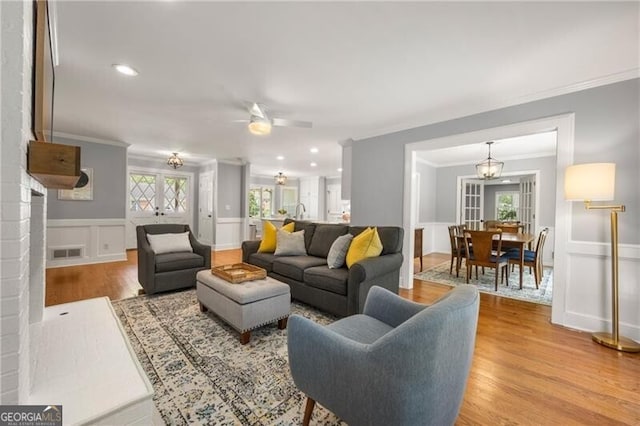 living area with crown molding, wainscoting, ceiling fan with notable chandelier, light wood finished floors, and a decorative wall