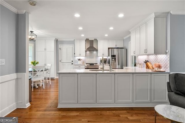 kitchen featuring wall chimney range hood, decorative backsplash, ornamental molding, stainless steel appliances, and white cabinetry
