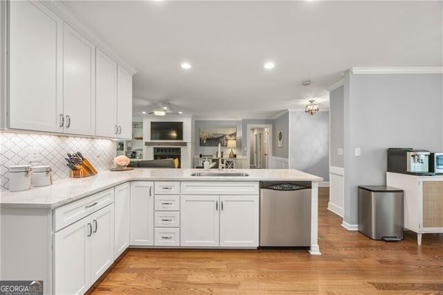 kitchen with dishwasher, a sink, white cabinets, a peninsula, and ornamental molding