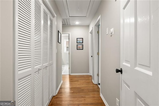 corridor featuring baseboards, wood finished floors, and attic access