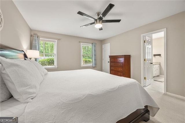 bedroom featuring baseboards, a ceiling fan, ensuite bathroom, and light carpet