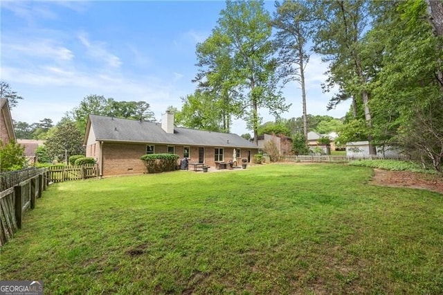 rear view of house featuring a lawn, brick siding, a chimney, and a fenced backyard