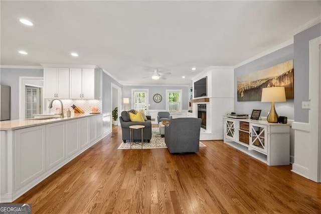 living room featuring a fireplace, a ceiling fan, recessed lighting, wood finished floors, and ornamental molding