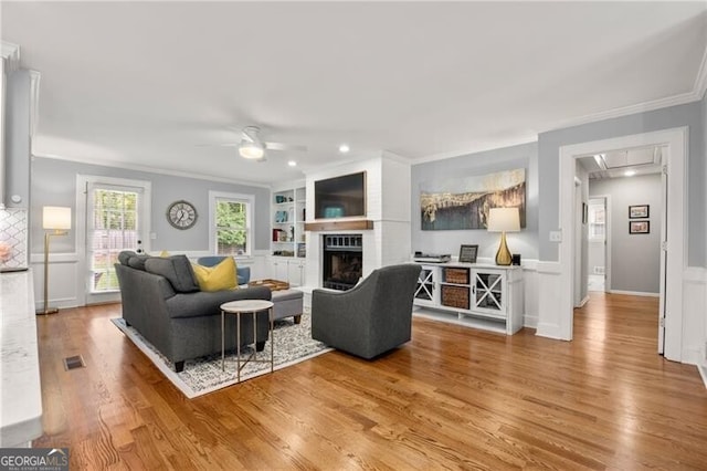 living area with ceiling fan, a fireplace, light wood-style flooring, attic access, and ornamental molding
