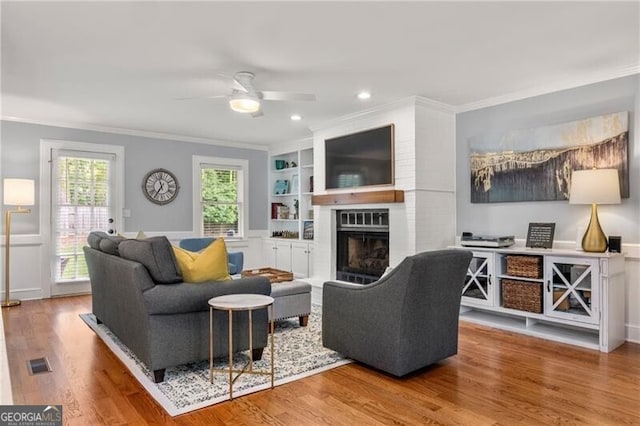 living area with crown molding, ceiling fan, visible vents, and a fireplace