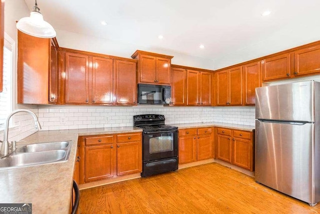 kitchen with decorative backsplash, light wood-style floors, light countertops, a sink, and black appliances