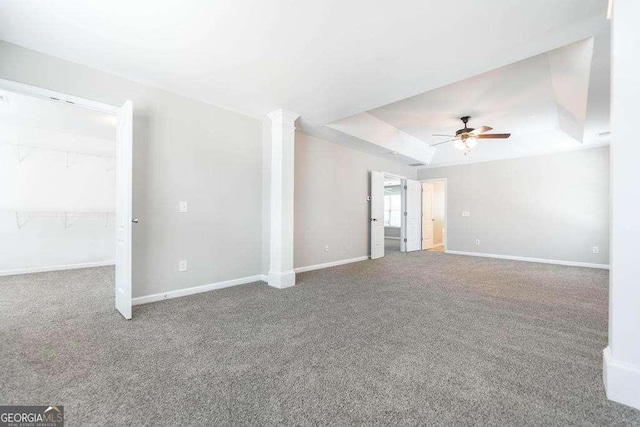 unfurnished living room featuring decorative columns, a ceiling fan, baseboards, a raised ceiling, and carpet flooring