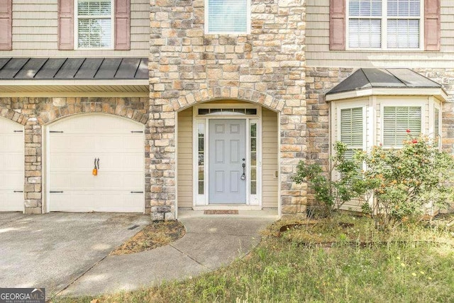 property entrance featuring an attached garage, stone siding, concrete driveway, a standing seam roof, and metal roof