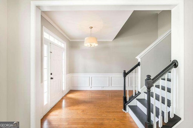 foyer entrance featuring crown molding, stairs, wood finished floors, and wainscoting