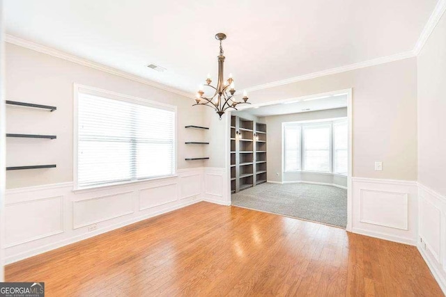 unfurnished dining area featuring visible vents, built in features, wood finished floors, a wainscoted wall, and a chandelier