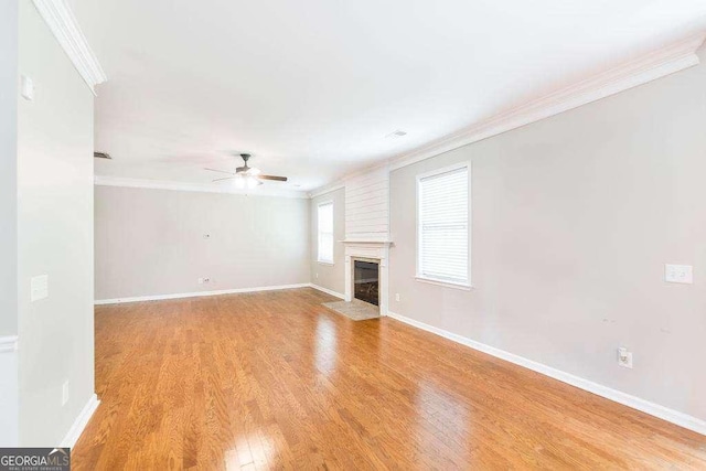 unfurnished living room featuring a ceiling fan, crown molding, a fireplace with flush hearth, baseboards, and light wood-style floors