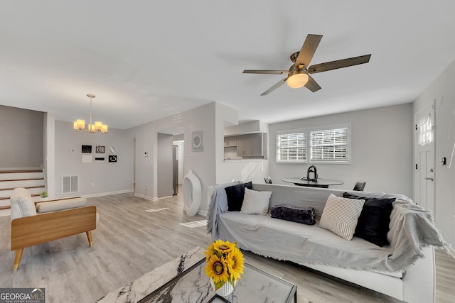 living area featuring ceiling fan with notable chandelier, stairs, baseboards, light wood-type flooring, and visible vents