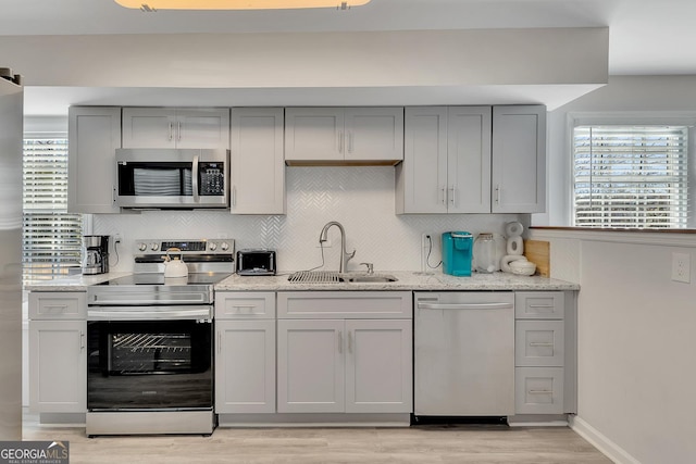 kitchen with backsplash, gray cabinetry, appliances with stainless steel finishes, and a sink