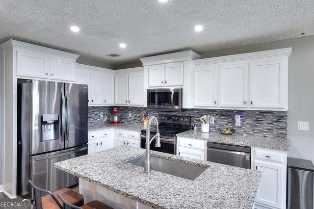 kitchen with a breakfast bar area, a textured ceiling, white cabinets, appliances with stainless steel finishes, and backsplash