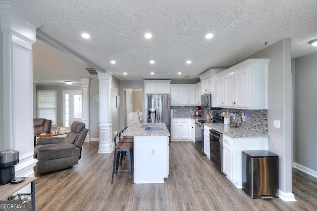 kitchen featuring a textured ceiling, a sink, baseboards, stainless steel appliances, and ornate columns