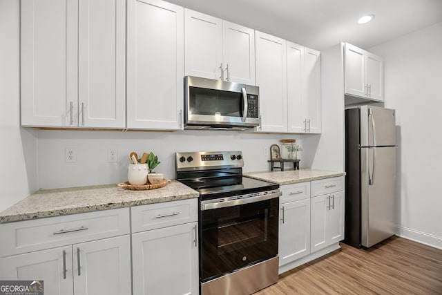 kitchen featuring recessed lighting, white cabinetry, light stone counters, light wood finished floors, and appliances with stainless steel finishes