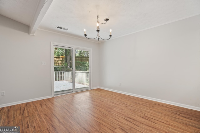 empty room featuring a chandelier, wood finished floors, baseboards, a textured ceiling, and crown molding