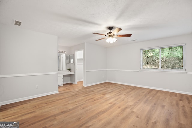 unfurnished room featuring ceiling fan, light wood finished floors, baseboards, and a textured ceiling
