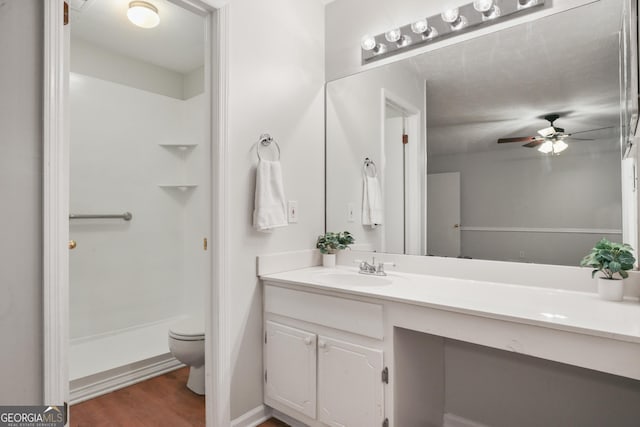 bathroom featuring toilet, a shower, vanity, wood finished floors, and ceiling fan