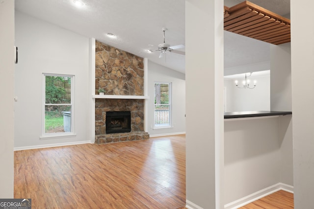 unfurnished living room with lofted ceiling, healthy amount of natural light, wood finished floors, baseboards, and a stone fireplace