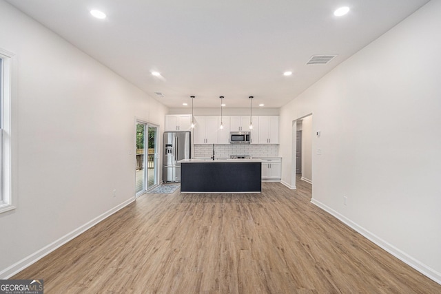 kitchen featuring white cabinets, an island with sink, light wood-style flooring, stainless steel appliances, and visible vents