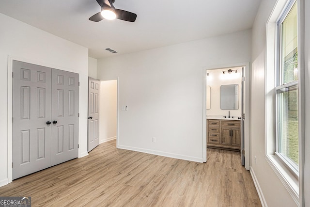 unfurnished bedroom featuring visible vents, a closet, light wood-style floors, baseboards, and ensuite bath