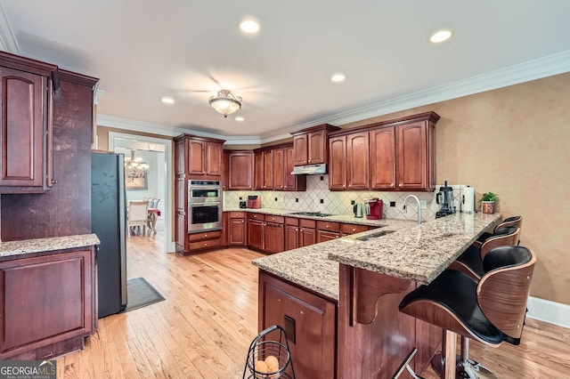 kitchen featuring appliances with stainless steel finishes, a breakfast bar, a peninsula, under cabinet range hood, and ornamental molding