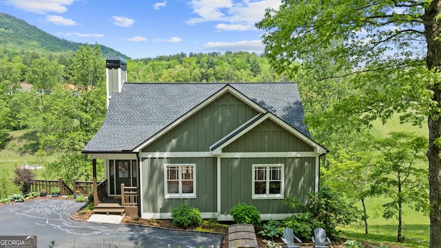 view of home's exterior featuring a shingled roof, board and batten siding, a chimney, and a forest view