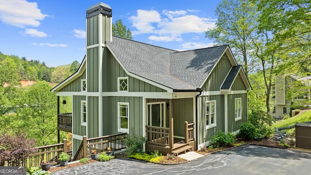 rear view of property featuring roof with shingles, board and batten siding, a chimney, and a porch