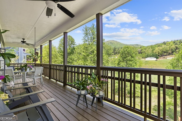 wooden terrace with outdoor dining area, a view of trees, and ceiling fan