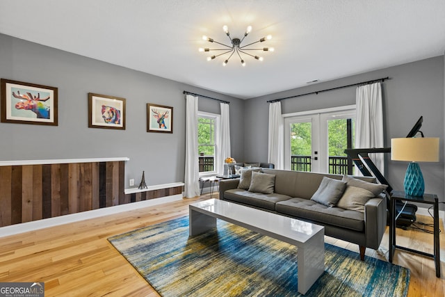 living area featuring an inviting chandelier, baseboards, wood finished floors, and french doors