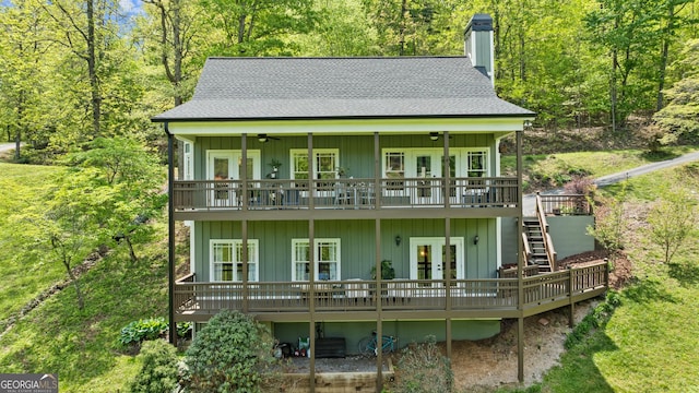 rear view of house featuring a deck, roof with shingles, french doors, a chimney, and stairway