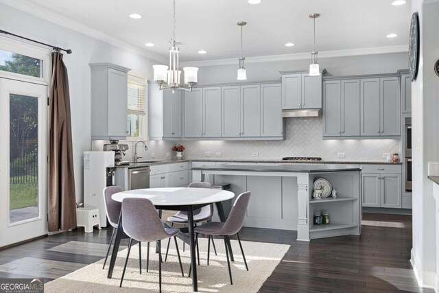 kitchen featuring an inviting chandelier, gray cabinets, under cabinet range hood, tasteful backsplash, and a sink