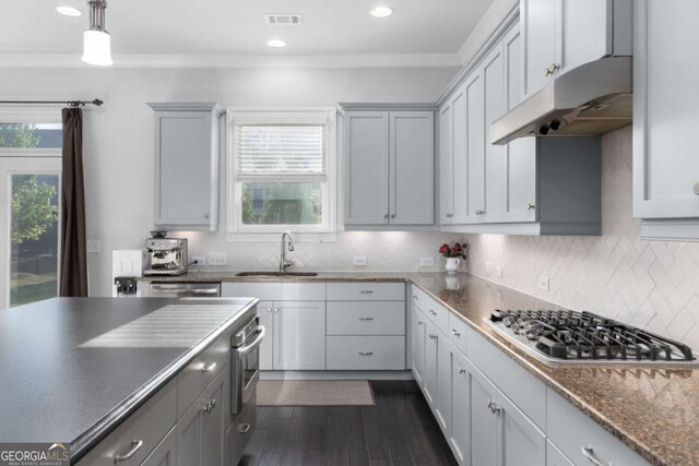 kitchen with dark countertops, appliances with stainless steel finishes, a sink, under cabinet range hood, and visible vents