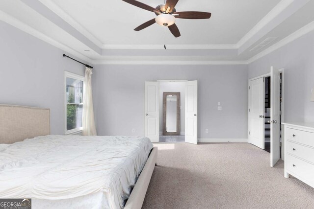 bedroom featuring crown molding, a tray ceiling, light carpet, and baseboards