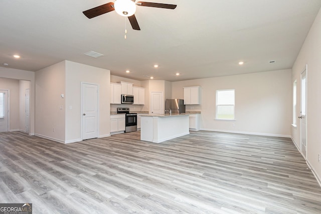 kitchen with light wood-style floors, an island with sink, stainless steel appliances, open floor plan, and baseboards