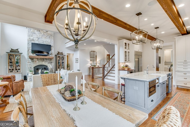dining room featuring light wood-style floors, a fireplace, beam ceiling, an inviting chandelier, and stairs