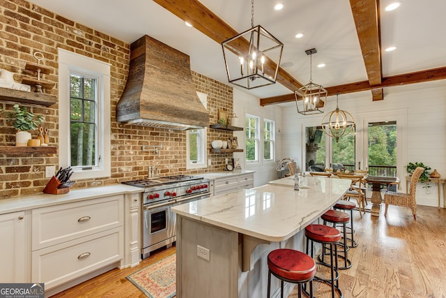kitchen featuring range with two ovens, beamed ceiling, custom exhaust hood, a notable chandelier, and light wood-style flooring